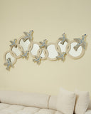 Decorative wall mirror with bird designs on a beige wall above a sofa.