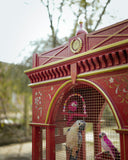 Decorative red birdcage with birds inside, set against a natural background.