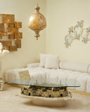 Living room with a glass coffee table featuring a decorative base, white sofa, and wall art.