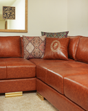 Brown leather sectional sofa with patterned and logo pillows in a room.