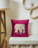 Red embroidered cushion with an elephant design on a wooden bench against a white wall.