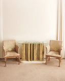 Decorative glass table with striped pattern flanked by two ornate chairs in a room with white walls and beige carpet.