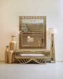 Decorative mirror with intricate patterns on a wall above a wicker bench with a cushion.