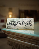 Decorative stone slab with urdu text on a reflective surface