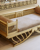 Decorative wooden bench with intricate carvings and beige cushions on a light background